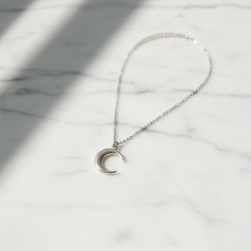 Dainty sterling silver crescent moon pendant necklace on white marble