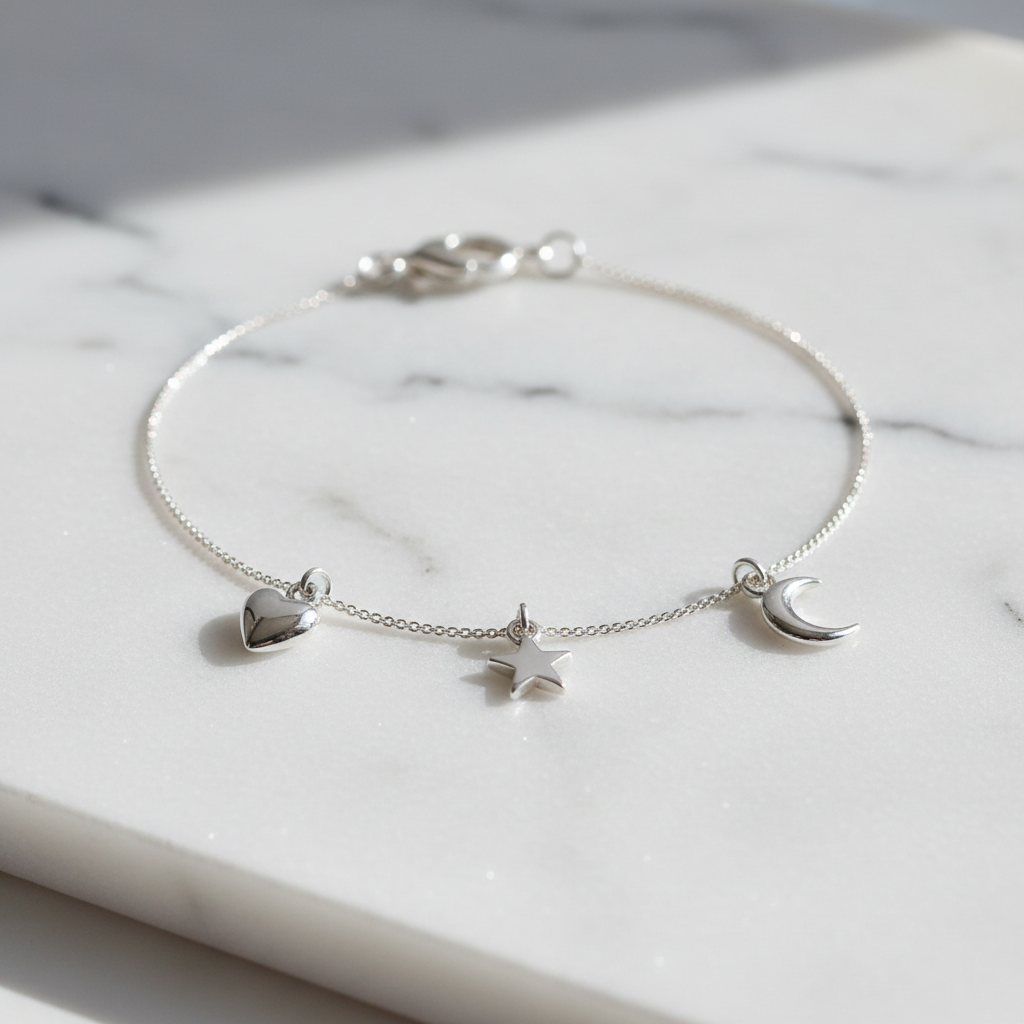 Delicate sterling silver charm bracelet with heart, star, and moon charms on white marble
